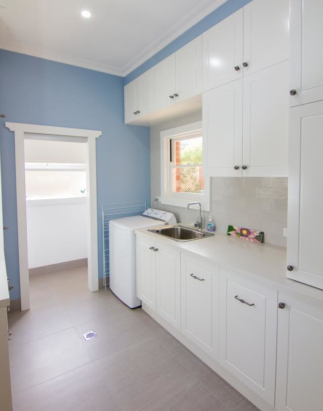 Esempio di una sala lavanderia tradizionale di medie dimensioni con lavello a vasca singola, ante in stile shaker, ante bianche, top in granito, pareti blu, pavimento in travertino, pavimento beige e lavasciuga