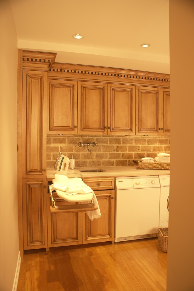 Inredning av ett klassiskt litet linjärt grovkök, med en enkel diskho, luckor med upphöjd panel, marmorbänkskiva, ljust trägolv, en tvättmaskin och torktumlare bredvid varandra, skåp i mellenmörkt trä och bruna väggar