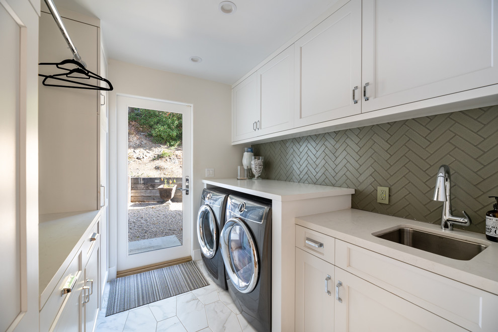 Klassisk inredning av en mycket stor parallell tvättstuga enbart för tvätt, med en undermonterad diskho, vita skåp, bänkskiva i kvarts och en tvättmaskin och torktumlare bredvid varandra