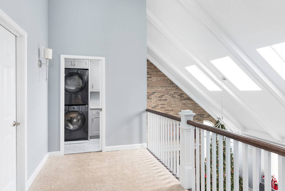 This is an example of a medium sized traditional l-shaped separated utility room in Chicago with recessed-panel cabinets, grey cabinets, engineered stone countertops, a stacked washer and dryer, white worktops, a submerged sink, grey walls, carpet and beige floors.