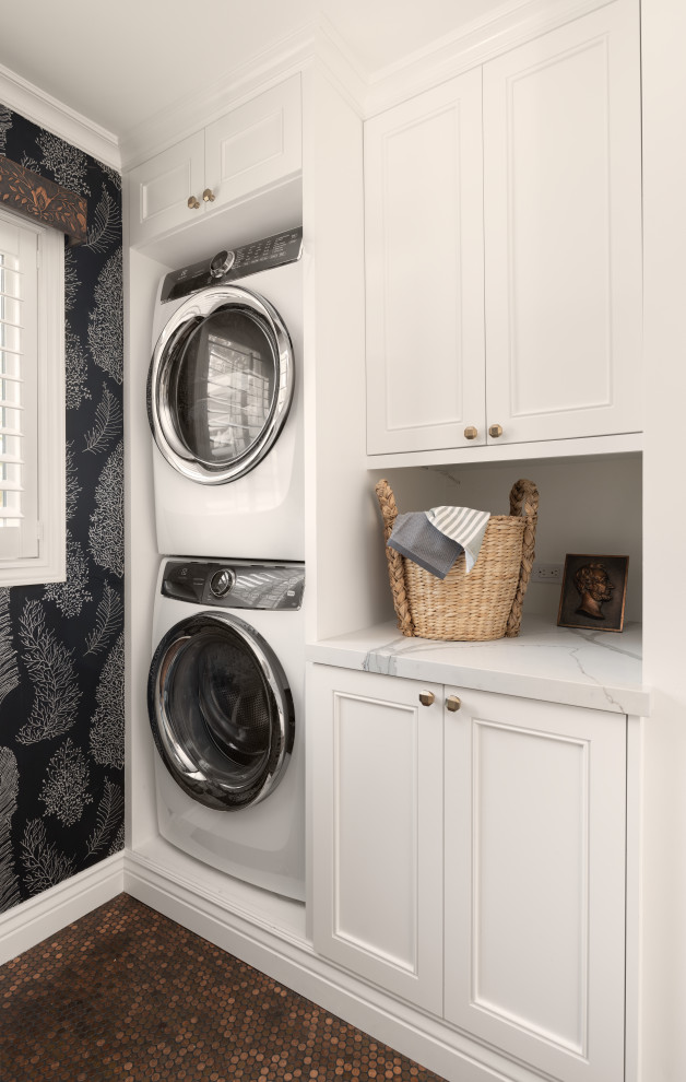 Ejemplo de lavadero tradicional renovado con armarios con paneles empotrados, puertas de armario blancas, paredes negras, lavadora y secadora apiladas, suelo marrón y encimeras blancas