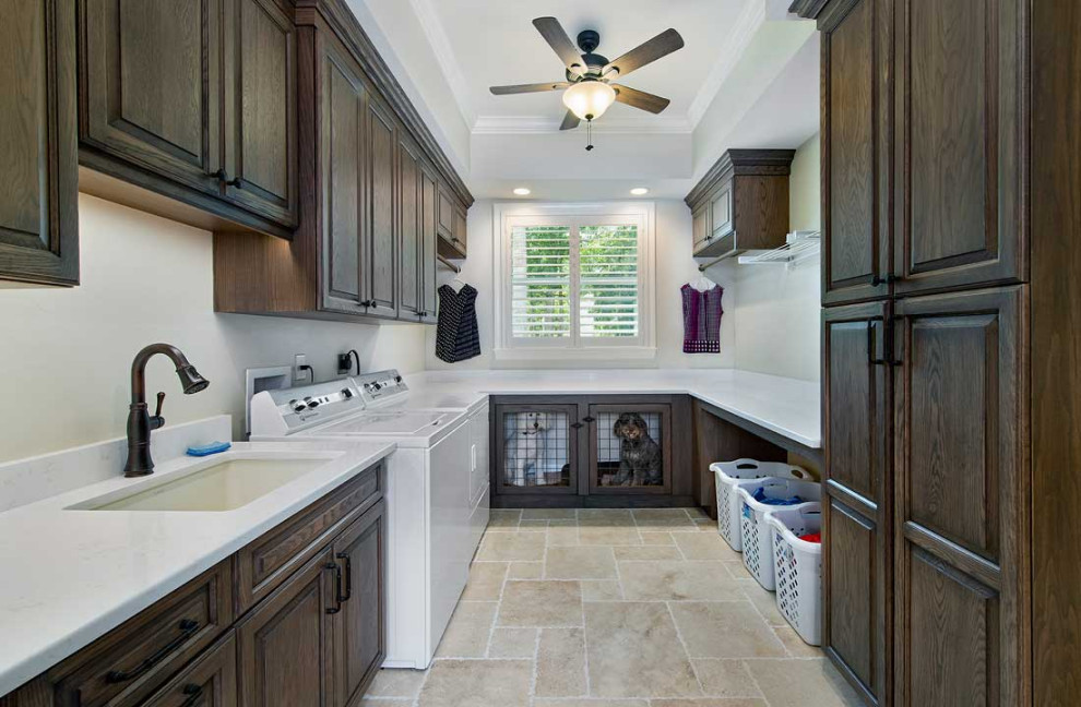 This is an example of a large classic u-shaped utility room in Miami with a submerged sink, raised-panel cabinets, dark wood cabinets, engineered stone countertops, beige splashback, beige walls, travertine flooring, a side by side washer and dryer, beige floors, white worktops and a drop ceiling.