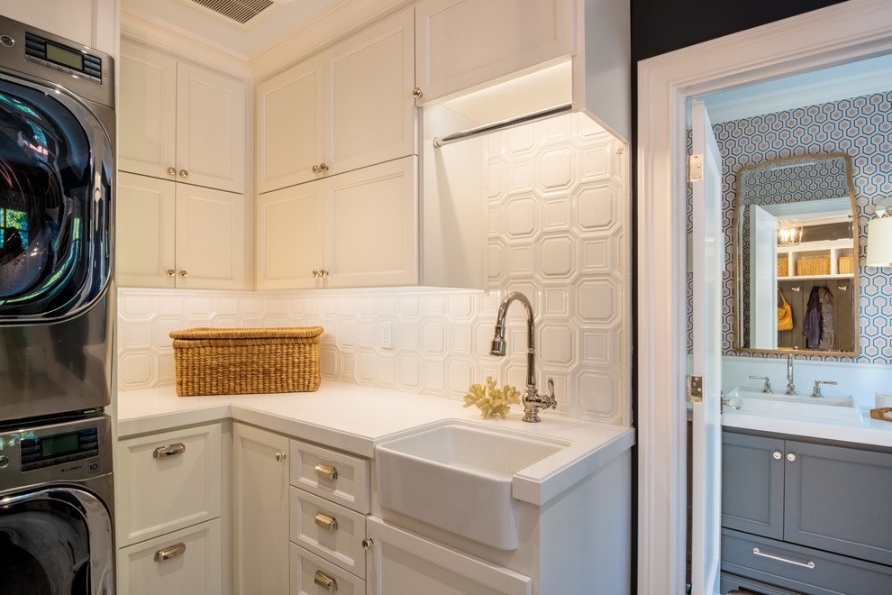 Inspiration for a large transitional u-shaped marble floor utility room remodel in San Francisco with a farmhouse sink, shaker cabinets, white cabinets, solid surface countertops, gray walls and a stacked washer/dryer