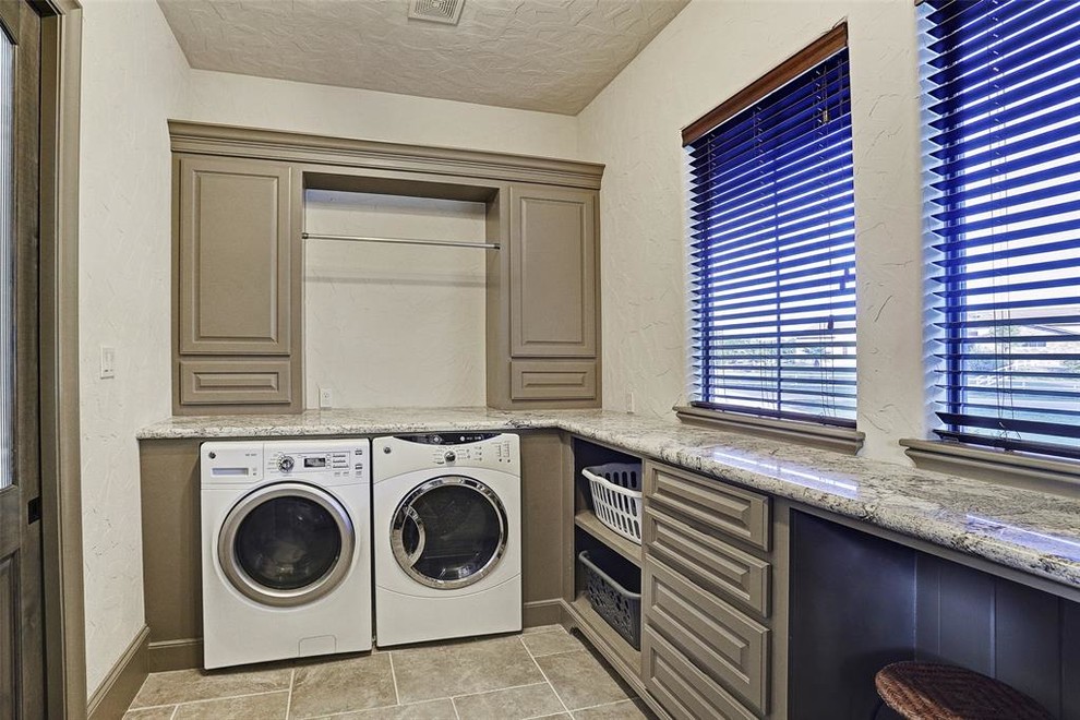 Example of a huge transitional u-shaped ceramic tile and beige floor utility room design in Houston with a single-bowl sink, raised-panel cabinets, gray cabinets, granite countertops, white walls, a side-by-side washer/dryer and gray countertops
