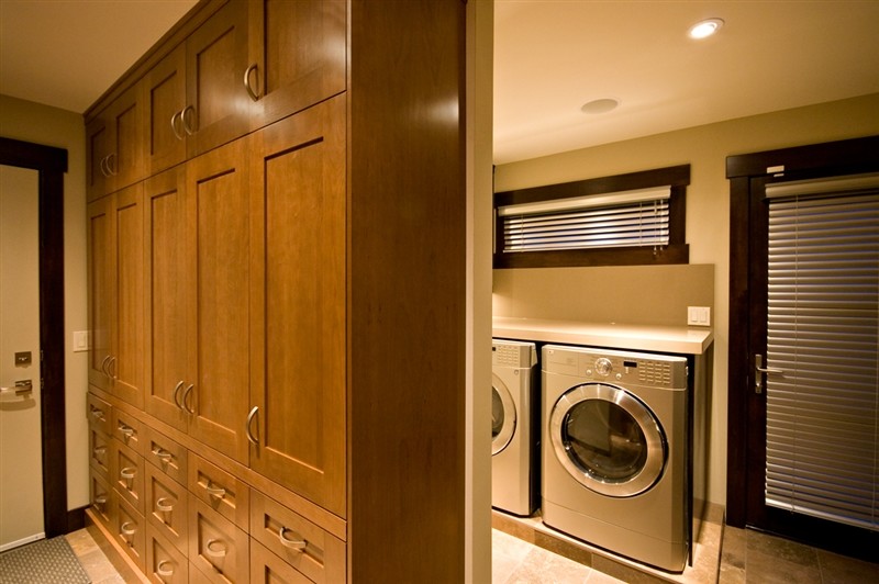 Inspiration for a large classic single-wall utility room in Calgary with a submerged sink, shaker cabinets, dark wood cabinets, engineered stone countertops, beige walls, travertine flooring and a side by side washer and dryer.