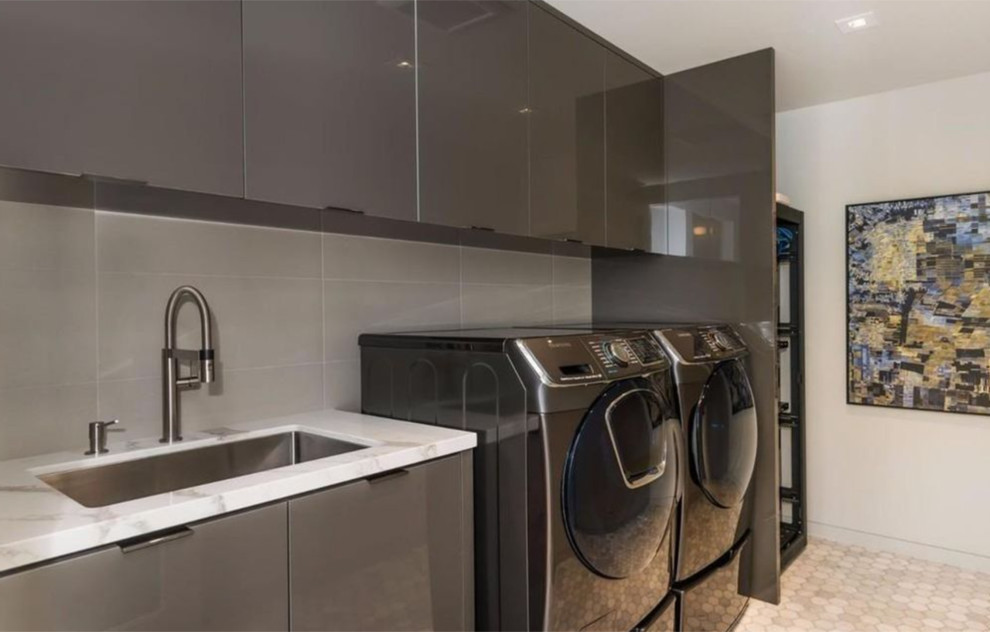 Example of a mid-sized trendy single-wall ceramic tile dedicated laundry room design in Boston with an undermount sink, flat-panel cabinets, gray cabinets, marble countertops, white walls and a side-by-side washer/dryer