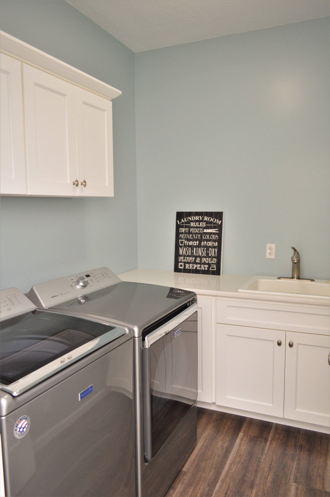 Klassisk inredning av en mellanstor vita l-formad vitt tvättstuga enbart för tvätt, med en nedsänkt diskho, skåp i shakerstil, vita skåp, bänkskiva i kvartsit, blå väggar, en tvättmaskin och torktumlare bredvid varandra och brunt golv
