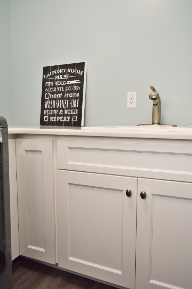 Foto på en mellanstor vintage vita l-formad tvättstuga enbart för tvätt, med en nedsänkt diskho, skåp i shakerstil, vita skåp, bänkskiva i kvartsit, blå väggar, en tvättmaskin och torktumlare bredvid varandra och brunt golv