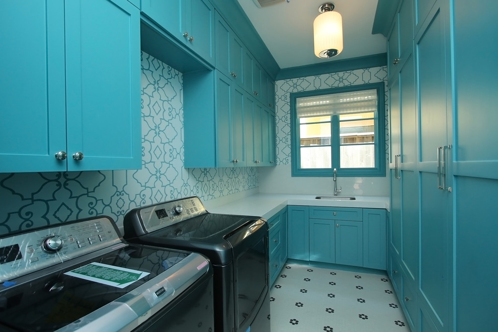 Exempel på en stor klassisk u-formad tvättstuga enbart för tvätt, med en undermonterad diskho, bänkskiva i kvartsit, en tvättmaskin och torktumlare bredvid varandra, luckor med infälld panel, blå skåp, flerfärgade väggar och klinkergolv i porslin