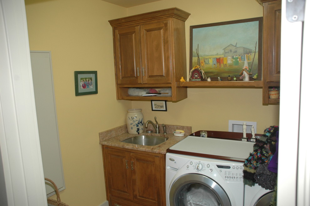 Bild på en liten vintage linjär tvättstuga enbart för tvätt, med en undermonterad diskho, luckor med upphöjd panel, skåp i mellenmörkt trä, granitbänkskiva, gula väggar, klinkergolv i keramik och en tvättmaskin och torktumlare bredvid varandra