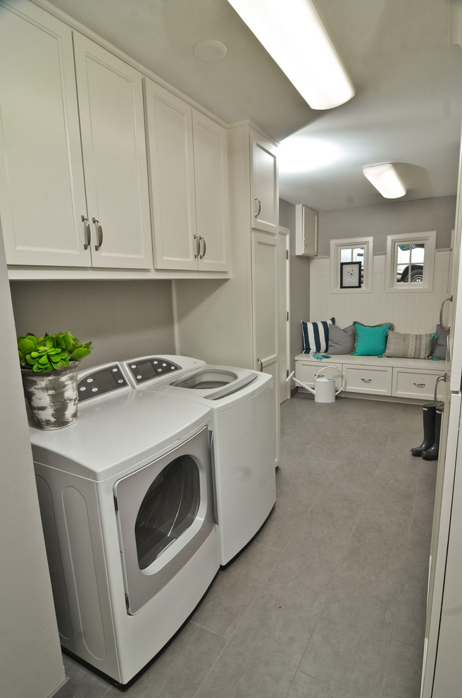 Klassisk inredning av en mellanstor l-formad liten tvättstuga, med luckor med infälld panel, vita skåp, grå väggar, klinkergolv i keramik, en tvättmaskin och torktumlare bredvid varandra och grått golv