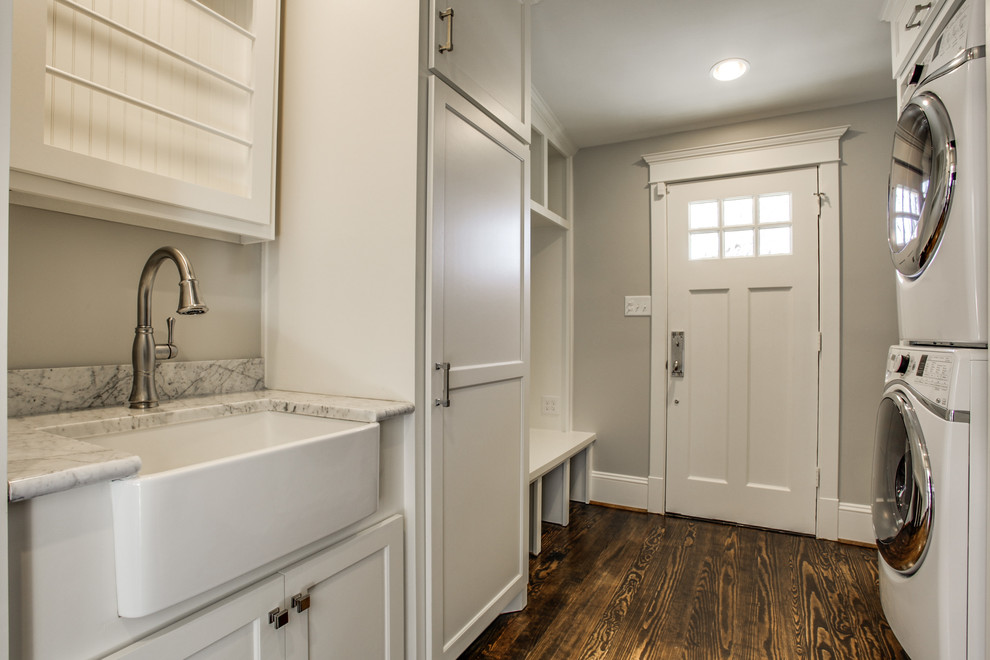 Large classic galley utility room in Dallas with a belfast sink, shaker cabinets, white cabinets, marble worktops, grey walls, dark hardwood flooring and a stacked washer and dryer.