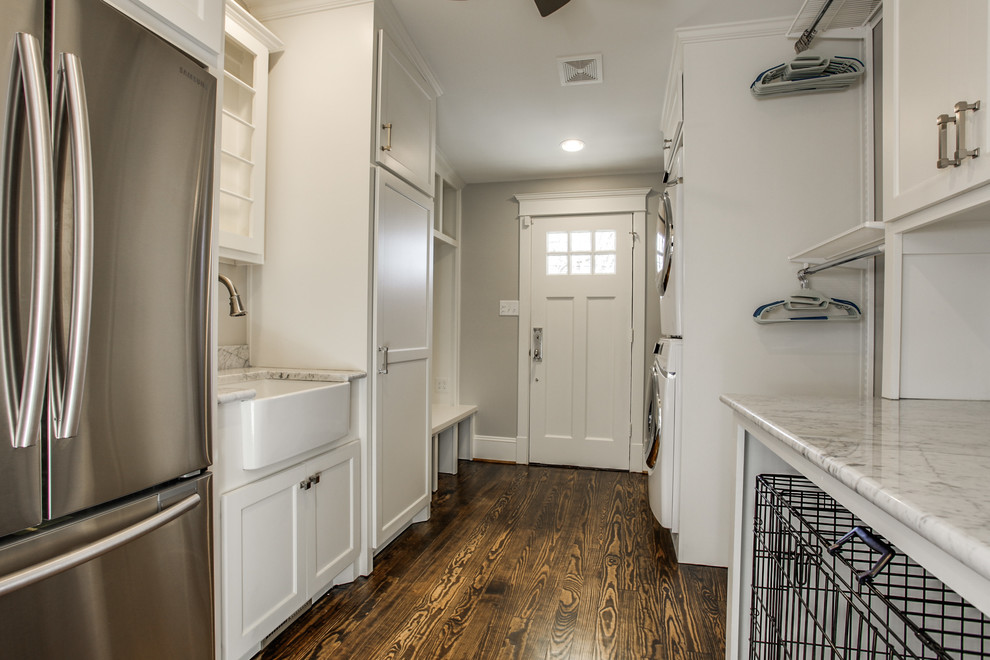 Large traditional galley utility room in Dallas with a belfast sink, shaker cabinets, white cabinets, marble worktops, grey walls, dark hardwood flooring, a stacked washer and dryer and white worktops.