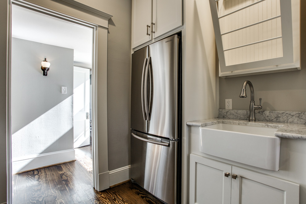 Inspiration for a large transitional galley dark wood floor utility room remodel in Dallas with a farmhouse sink, shaker cabinets, white cabinets, marble countertops, gray walls and a stacked washer/dryer