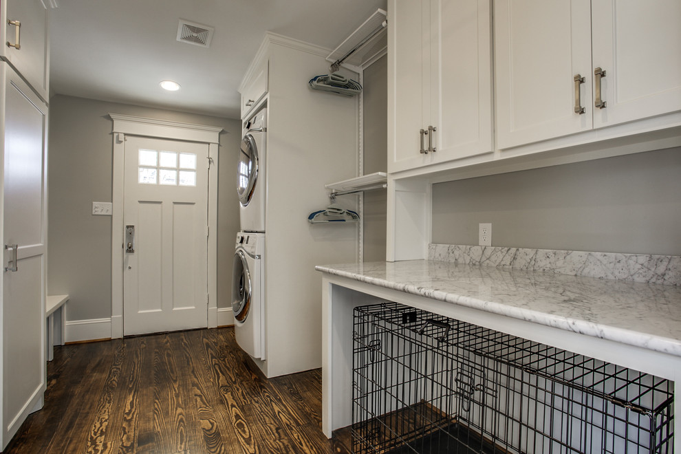 This is an example of a large traditional galley utility room in Dallas with shaker cabinets, white cabinets, marble worktops, grey walls, dark hardwood flooring, a stacked washer and dryer and white worktops.
