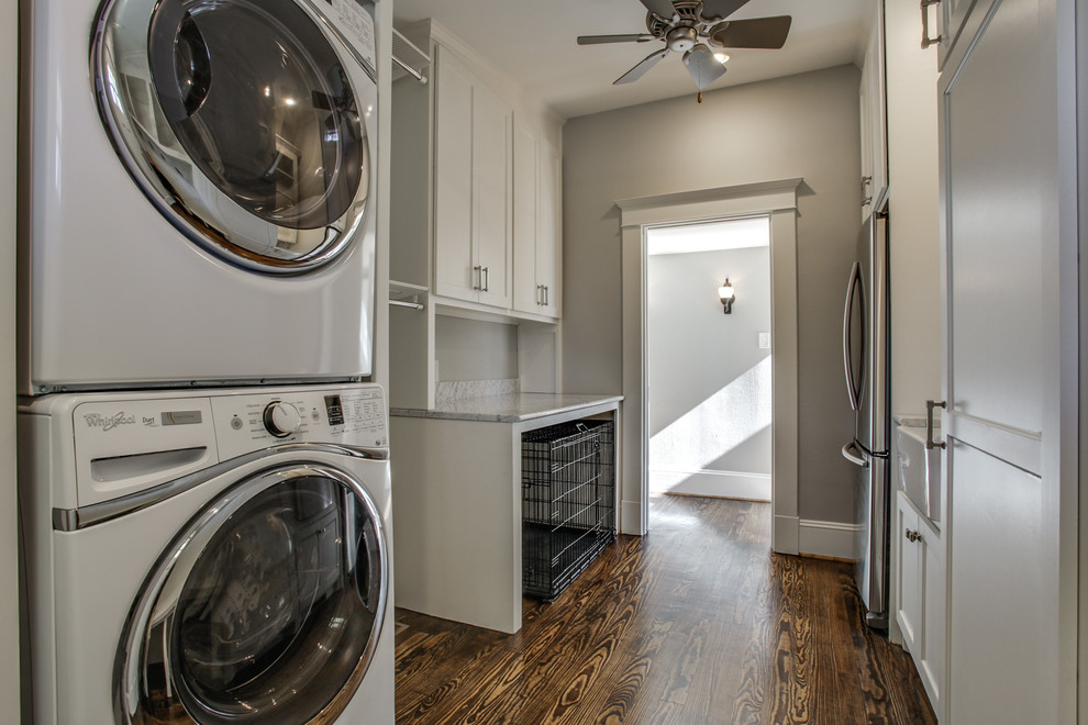 Inspiration for a large traditional galley utility room in Dallas with a belfast sink, shaker cabinets, white cabinets, marble worktops, grey walls, dark hardwood flooring and a stacked washer and dryer.