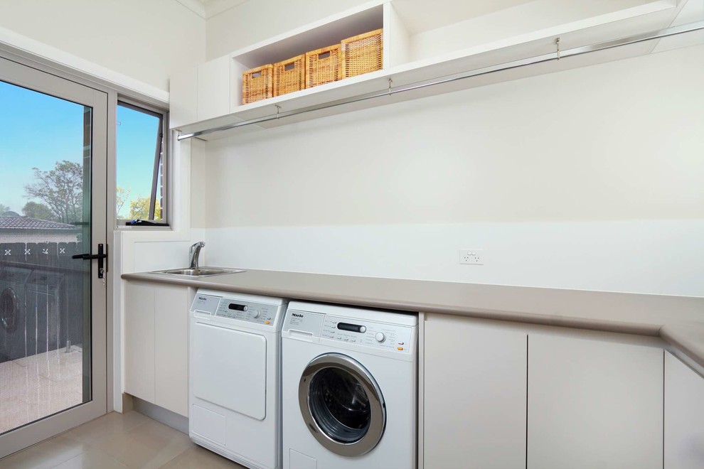 Immagine di una sala lavanderia minimalista di medie dimensioni con lavello da incasso, ante beige, top in laminato, pareti beige, pavimento in gres porcellanato, lavatrice e asciugatrice affiancate e ante lisce