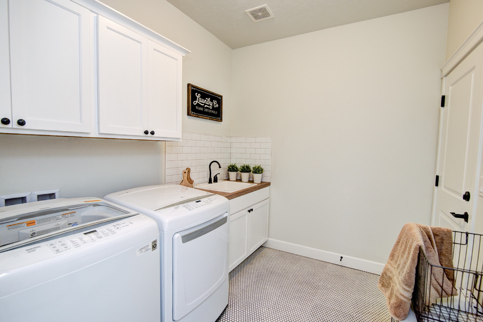 Example of a mid-sized mountain style galley ceramic tile and beige floor dedicated laundry room design in Other with a drop-in sink, shaker cabinets, white cabinets, laminate countertops, white walls and a side-by-side washer/dryer