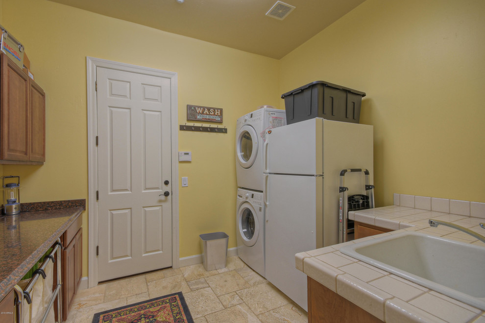 На фото: большая п-образная универсальная комната с желтыми стенами, с сушильной машиной на стиральной машине, коричневым полом и разноцветной столешницей