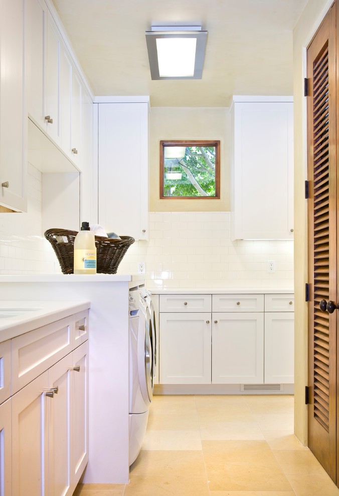Dedicated laundry room - large tropical l-shaped travertine floor and brown floor dedicated laundry room idea in Santa Barbara with an undermount sink, shaker cabinets, white cabinets, beige walls, a side-by-side washer/dryer and white countertops
