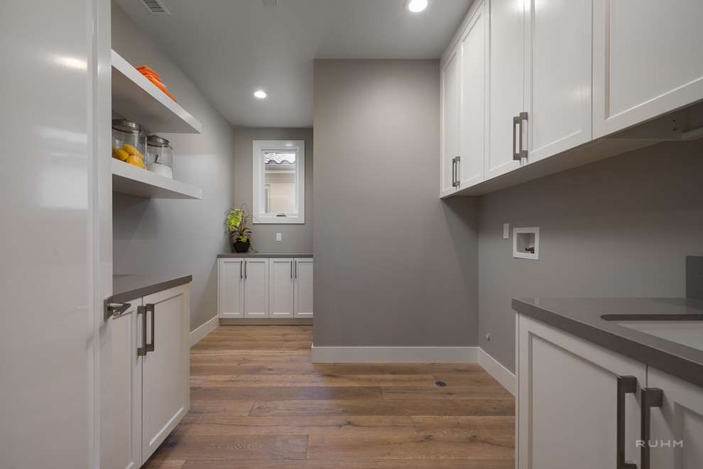 Foto di una sala lavanderia design con ante in stile shaker, ante bianche, top in quarzo composito, pareti grigie e pavimento in legno massello medio