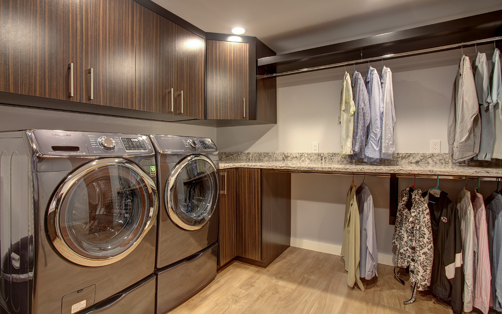 Exempel på en stor modern u-formad tvättstuga enbart för tvätt, med släta luckor, skåp i mörkt trä, bänkskiva i koppar, vita väggar, ljust trägolv och en tvättmaskin och torktumlare bredvid varandra