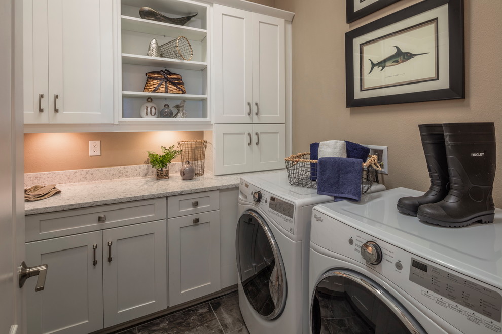 Idéer för mellanstora amerikanska linjära vitt tvättstugor enbart för tvätt, med skåp i shakerstil, grå skåp, granitbänkskiva, bruna väggar och en tvättmaskin och torktumlare bredvid varandra