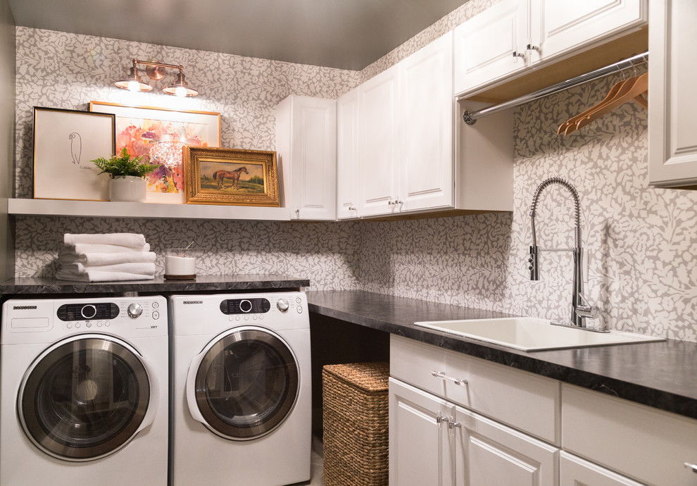 Imagen de cuarto de lavado en L tradicional con fregadero encastrado, armarios con paneles con relieve, puertas de armario blancas, paredes grises, lavadora y secadora juntas y encimeras negras