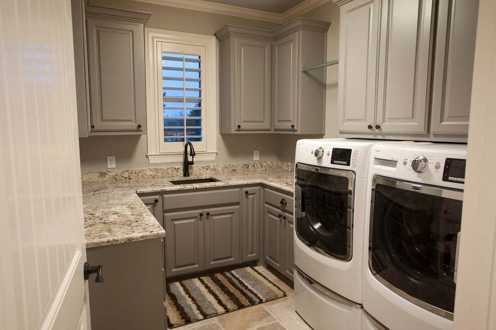 Mittelgroße Klassische Waschküche in U-Form mit Unterbauwaschbecken, Schrankfronten mit vertiefter Füllung, grauen Schränken, Granit-Arbeitsplatte, grauer Wandfarbe, Travertin und Waschmaschine und Trockner nebeneinander in Austin