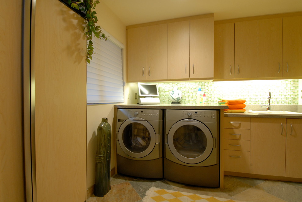 Modern inredning av en l-formad tvättstuga, med en rustik diskho, linoleumgolv, en tvättmaskin och torktumlare bredvid varandra, släta luckor och beige väggar