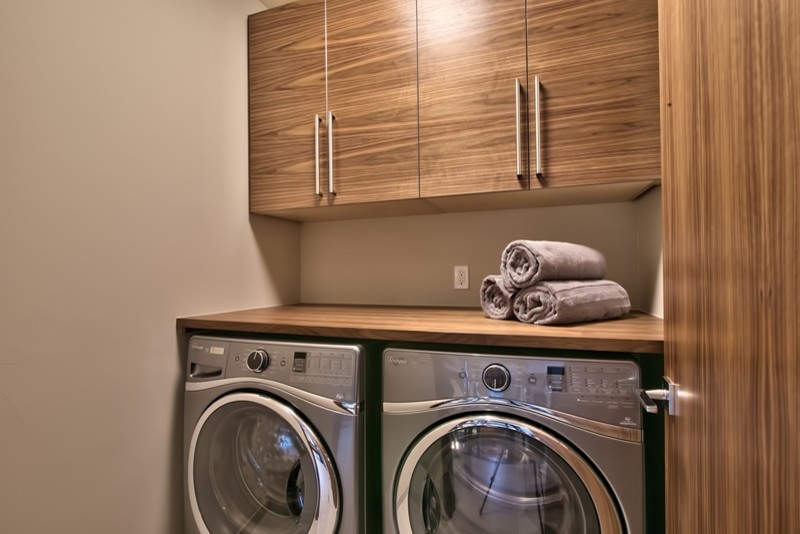 Diseño de armario lavadero lineal contemporáneo pequeño con armarios con paneles lisos, puertas de armario de madera oscura, encimera de madera, paredes beige, lavadora y secadora juntas y encimeras marrones