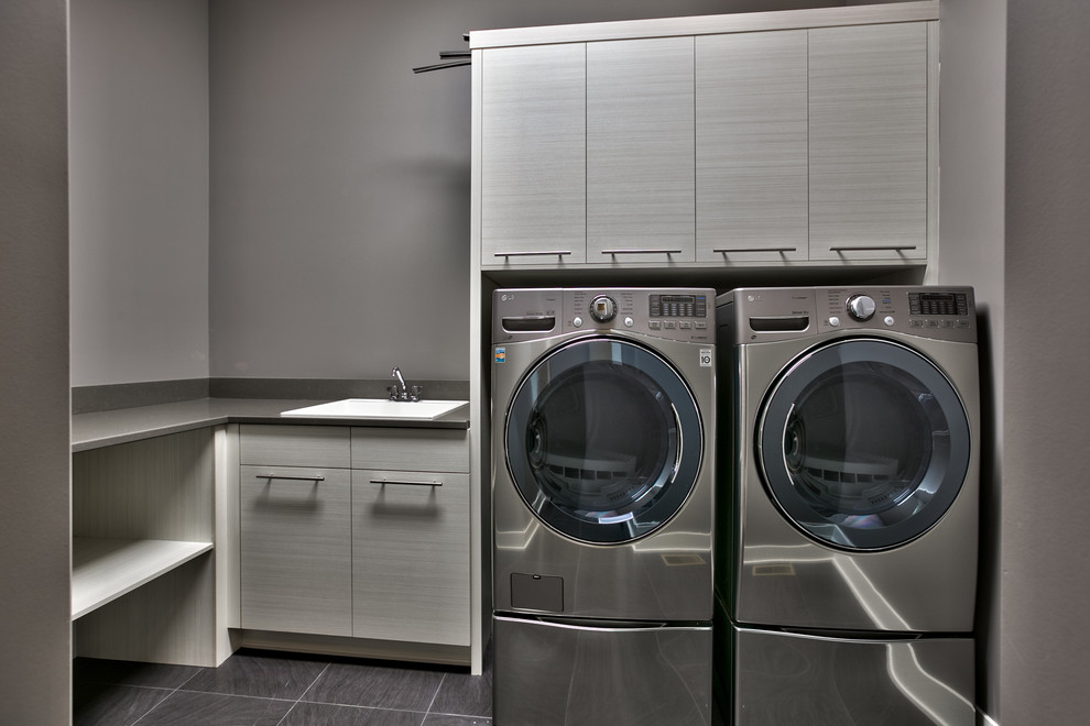 Immagine di una grande sala lavanderia minimalista con lavello da incasso, ante lisce, ante bianche, top in quarzite, pareti grigie, pavimento in vinile e lavatrice e asciugatrice affiancate