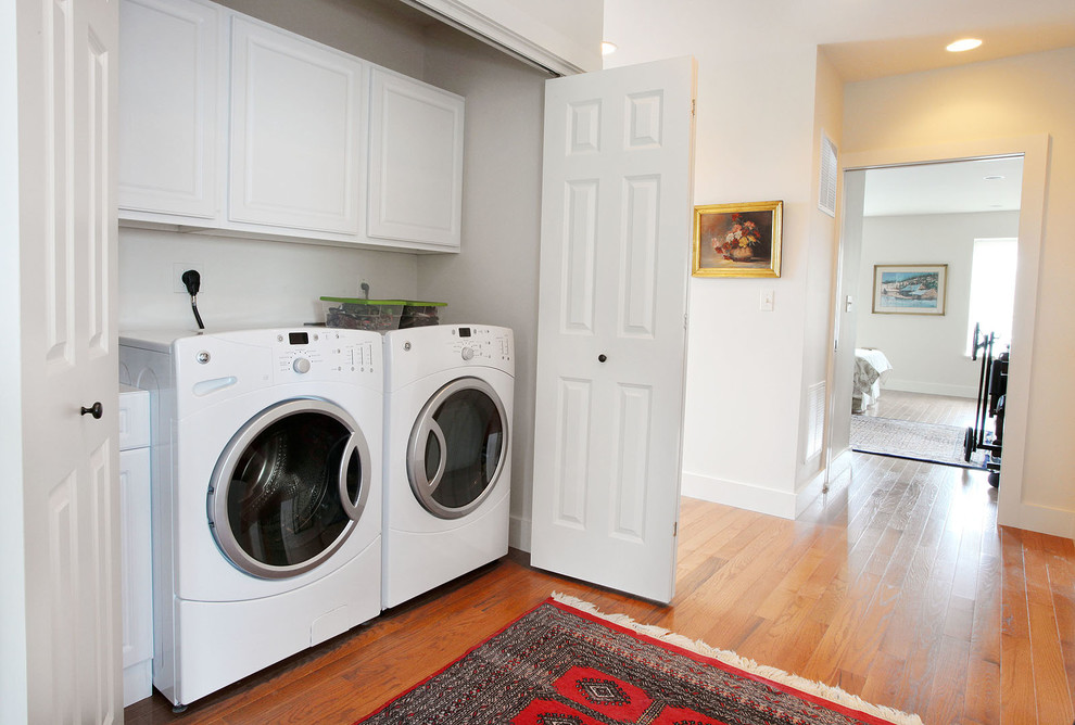 Foto di un piccolo ripostiglio-lavanderia tradizionale con ante con bugna sagomata, ante bianche, pavimento in legno massello medio, lavatrice e asciugatrice affiancate e pavimento marrone