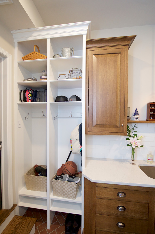 Photo of a medium sized traditional u-shaped utility room in Philadelphia with a submerged sink, raised-panel cabinets, medium wood cabinets, engineered stone countertops, grey walls, brick flooring and a stacked washer and dryer.