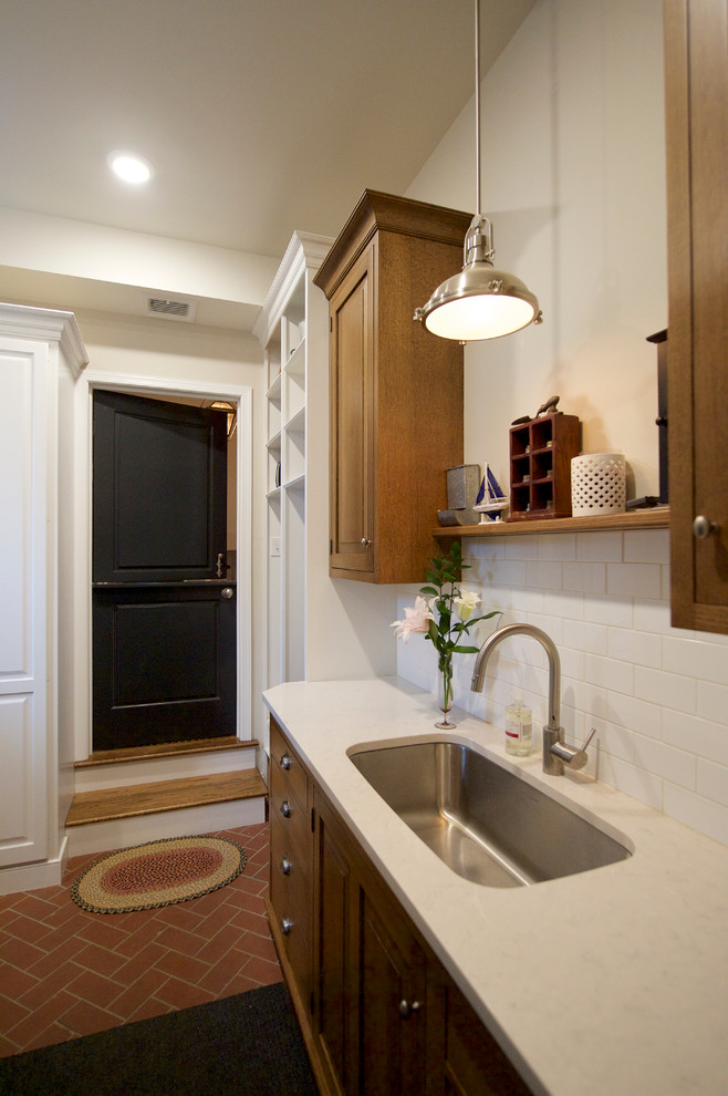 Inspiration for a mid-sized timeless u-shaped brick floor utility room remodel in Philadelphia with an undermount sink, raised-panel cabinets, medium tone wood cabinets, quartz countertops, gray walls and a stacked washer/dryer