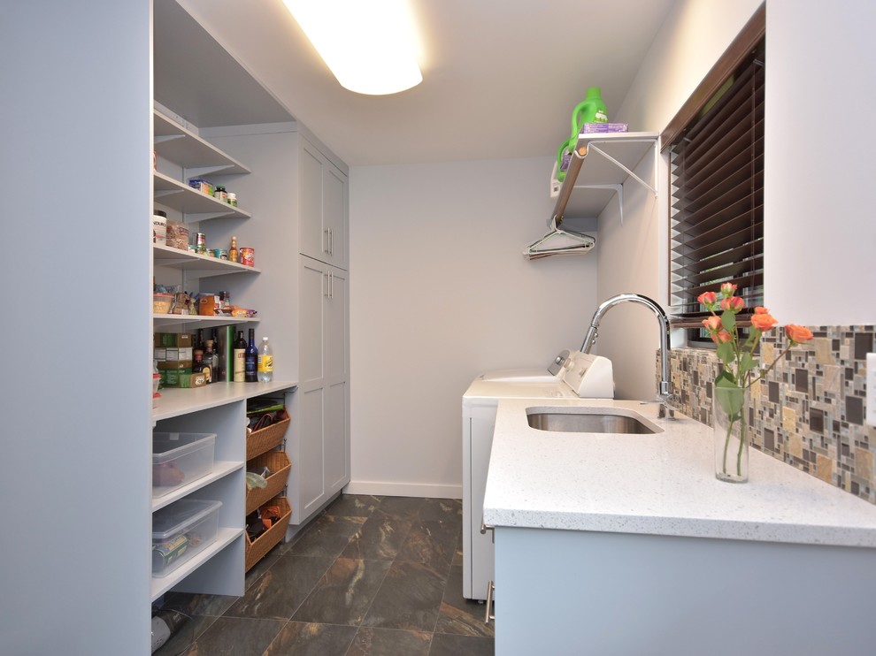 Foto på ett mellanstort funkis parallellt grovkök, med en undermonterad diskho, luckor med infälld panel, grå skåp, bänkskiva i kvartsit, grå väggar, skiffergolv och en tvättmaskin och torktumlare bredvid varandra