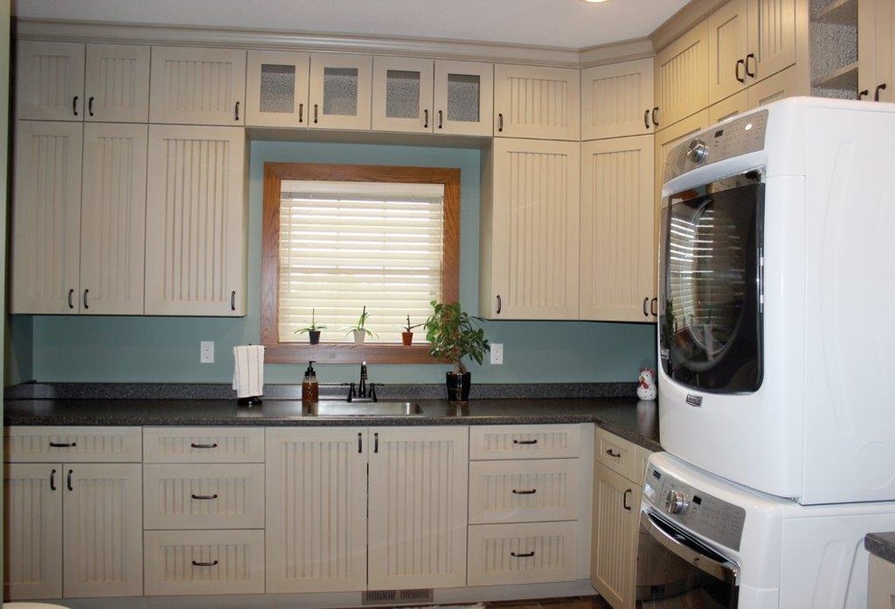This is an example of a large country l-shaped utility room in Cedar Rapids with beaded cabinets, white cabinets, laminate countertops, a built-in sink and a stacked washer and dryer.