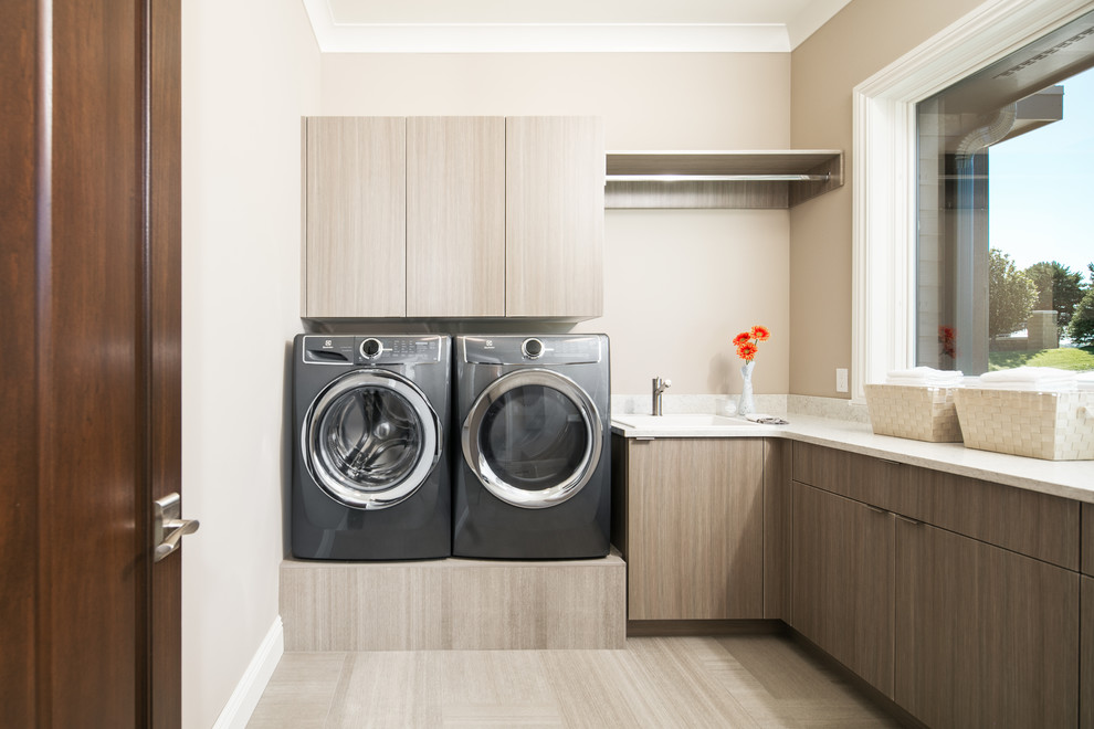 Foto på en mellanstor vintage l-formad tvättstuga enbart för tvätt, med en nedsänkt diskho, släta luckor, klinkergolv i porslin, en tvättmaskin och torktumlare bredvid varandra, brunt golv, grå skåp och beige väggar