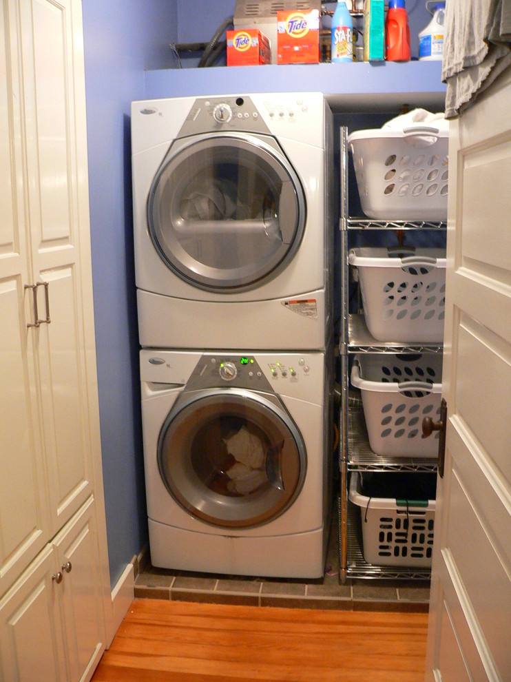 Kleine Klassische Waschküche mit lila Wandfarbe, hellem Holzboden und Waschmaschine und Trockner gestapelt in Sonstige