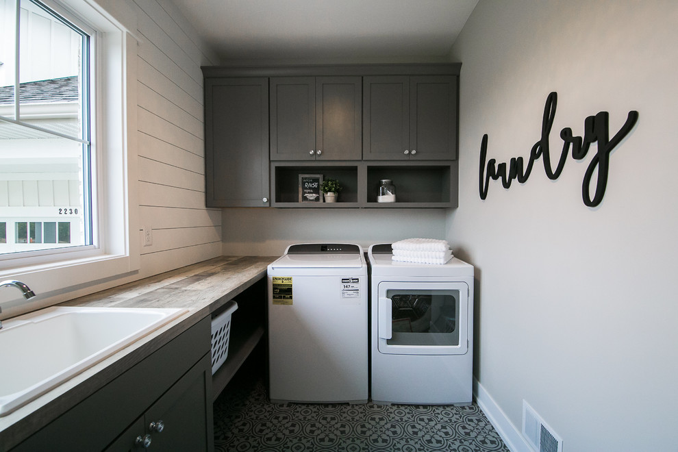 Inspiration for a mid-sized farmhouse l-shaped linoleum floor and gray floor dedicated laundry room remodel in Grand Rapids with a drop-in sink, shaker cabinets, gray cabinets, laminate countertops, gray walls, a side-by-side washer/dryer and brown countertops