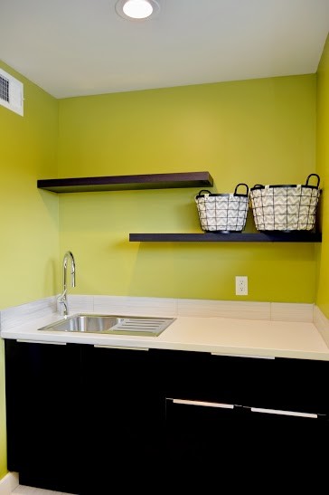 Foto di una sala lavanderia moderna di medie dimensioni con lavello da incasso, ante lisce, ante in legno bruno, top in granito, pareti gialle, pavimento con piastrelle in ceramica e lavatrice e asciugatrice affiancate