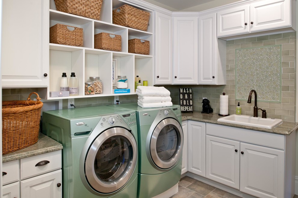 Klassisk inredning av en beige beige tvättstuga, med vita skåp, en tvättmaskin och torktumlare bredvid varandra och grå väggar