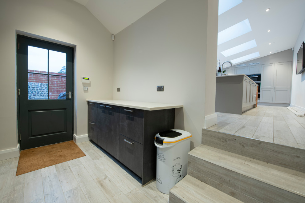 Immagine di una lavanderia moderna di medie dimensioni con ante lisce, ante nere, top in superficie solida, pavimento in gres porcellanato, lavatrice e asciugatrice nascoste e top bianco