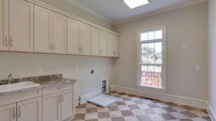 This is an example of a large traditional galley utility room in DC Metro with a built-in sink, recessed-panel cabinets, light wood cabinets, granite worktops, beige walls, travertine flooring and a side by side washer and dryer.