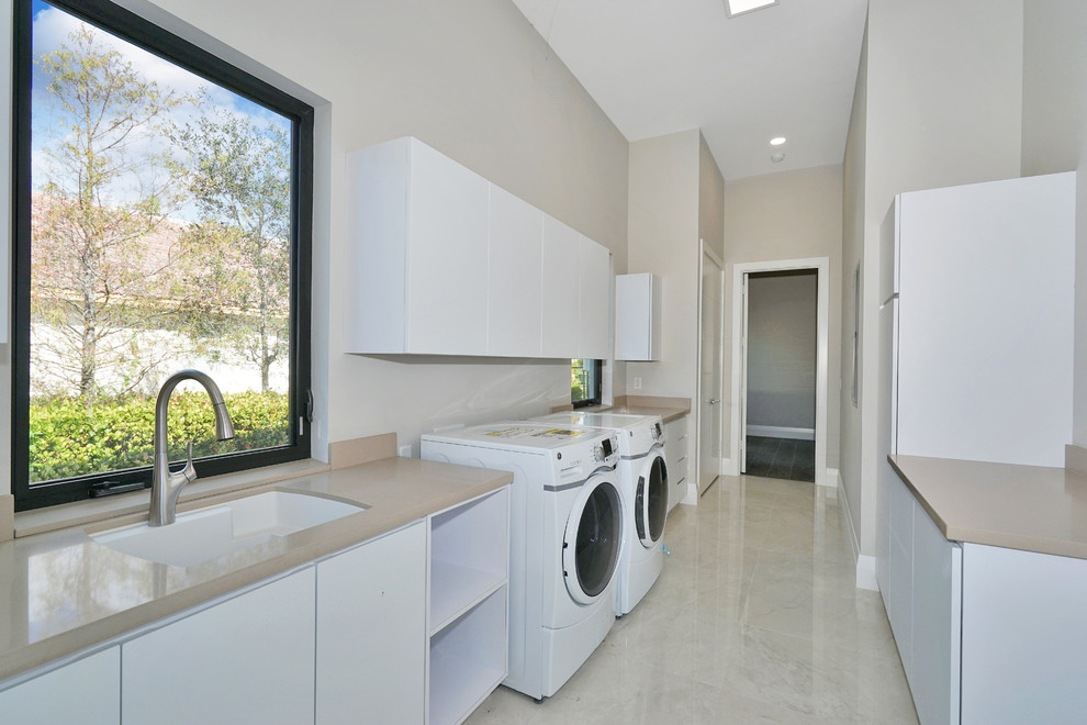 Inspiration for a large modern galley separated utility room in Miami with a submerged sink, flat-panel cabinets, white cabinets, marble worktops, beige walls, marble flooring, a side by side washer and dryer and beige floors.