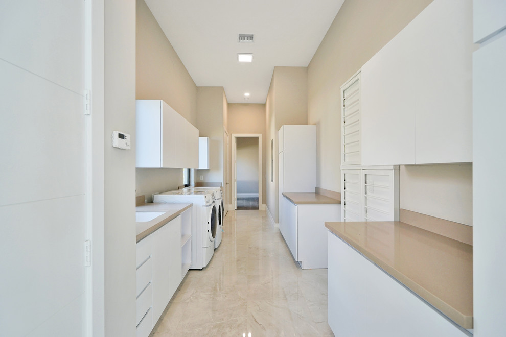 Dedicated laundry room - large modern galley marble floor and beige floor dedicated laundry room idea in Miami with an undermount sink, flat-panel cabinets, white cabinets, marble countertops, beige walls and a side-by-side washer/dryer
