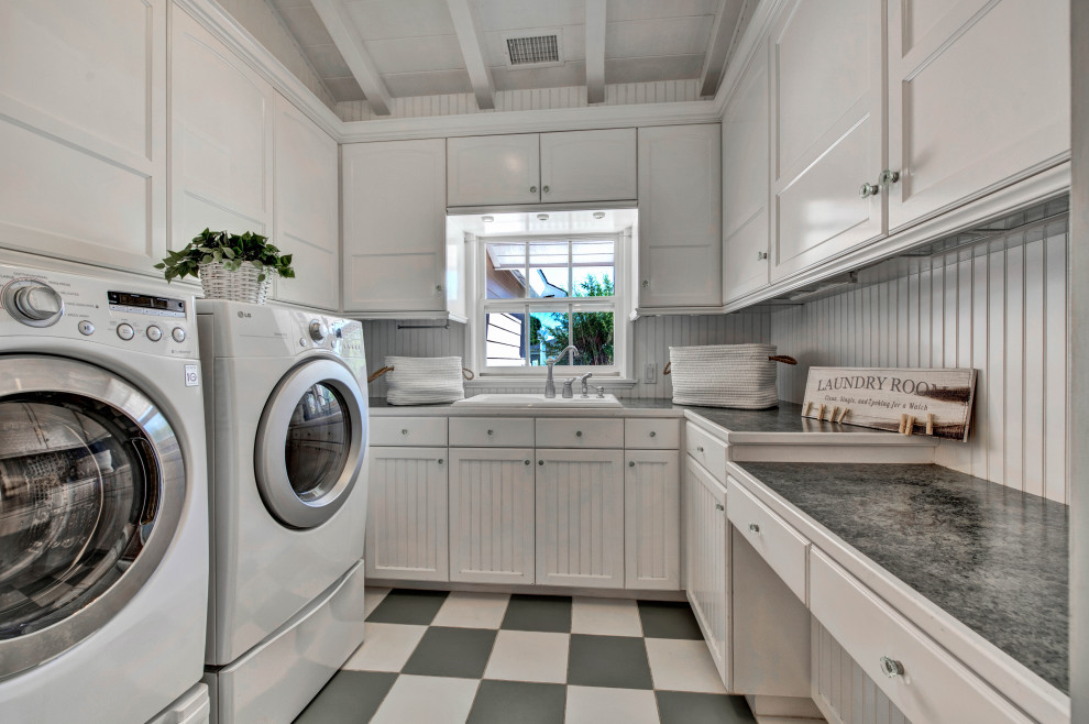 Klassische Waschküche mit Einbauwaschbecken, Schrankfronten mit vertiefter Füllung, weißen Schränken, weißer Wandfarbe, Waschmaschine und Trockner nebeneinander, buntem Boden und schwarzer Arbeitsplatte in Orange County