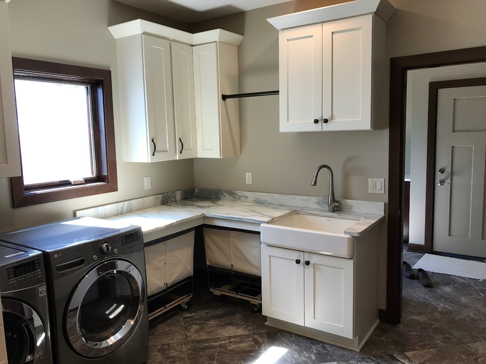 Example of a mid-sized classic l-shaped dark wood floor and brown floor dedicated laundry room design in Milwaukee with a farmhouse sink, shaker cabinets, white cabinets, marble countertops, beige walls, a side-by-side washer/dryer and gray countertops