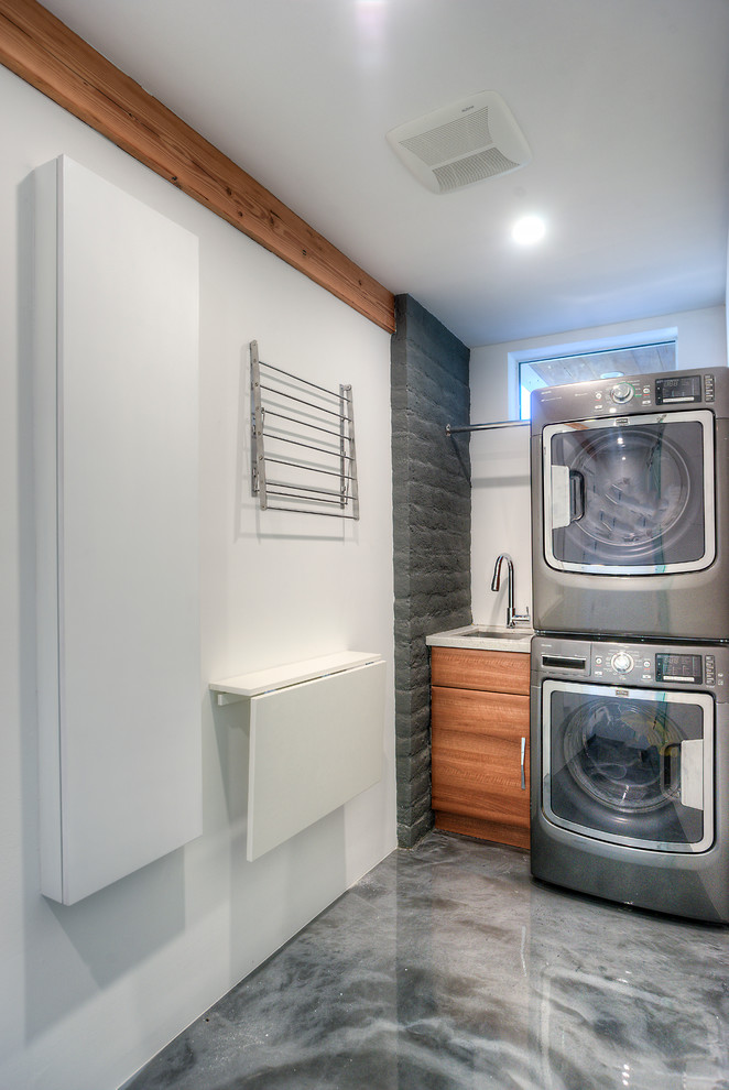 Exempel på en mellanstor modern tvättstuga, med vita väggar, betonggolv, en tvättpelare, släta luckor, skåp i mellenmörkt trä, bänkskiva i kvartsit och en undermonterad diskho
