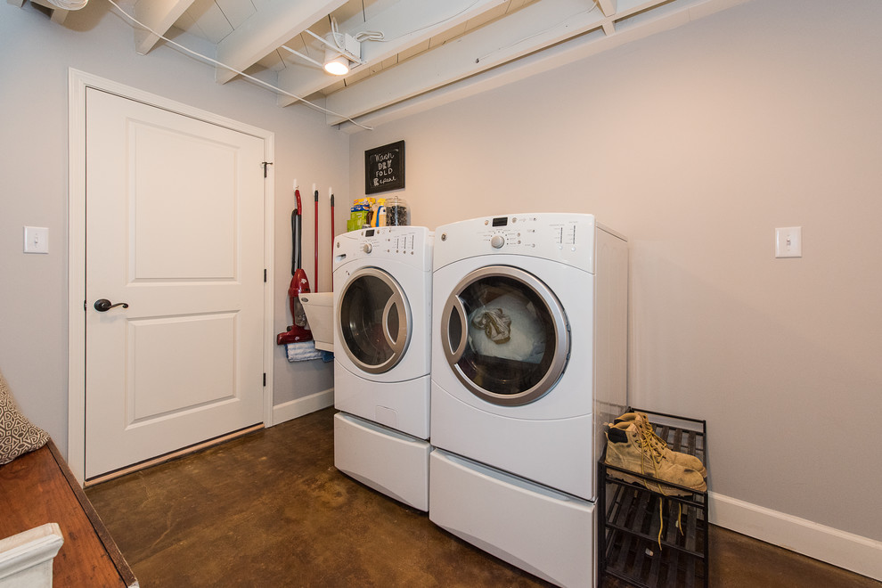 Exempel på en stor klassisk parallell tvättstuga enbart för tvätt, med en tvättmaskin och torktumlare bredvid varandra, träbänkskiva, grå väggar och betonggolv